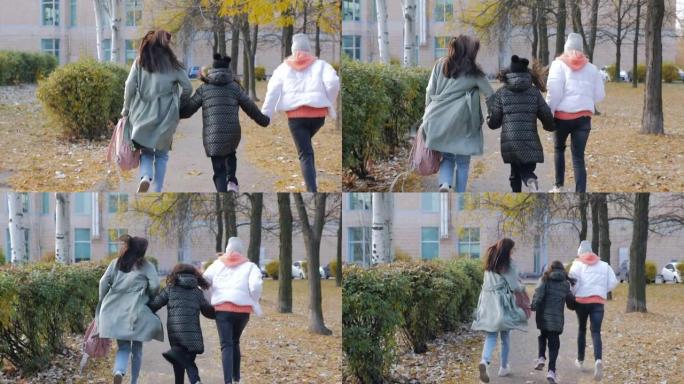 一个有两个女儿的女人急忙上学，从女孩的后面和母亲一起沿着秋天的小巷奔跑。