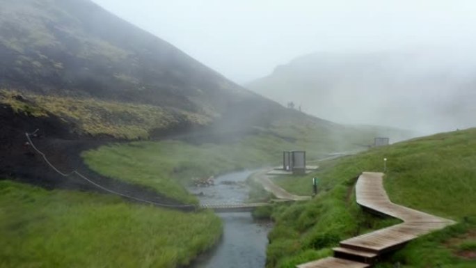雷克雅达勒河谷的鸟瞰图，温泉河和游泳池，郁郁葱葱的绿草草地和带有地热蒸汽的山丘。在冰岛的温泉中沐浴的