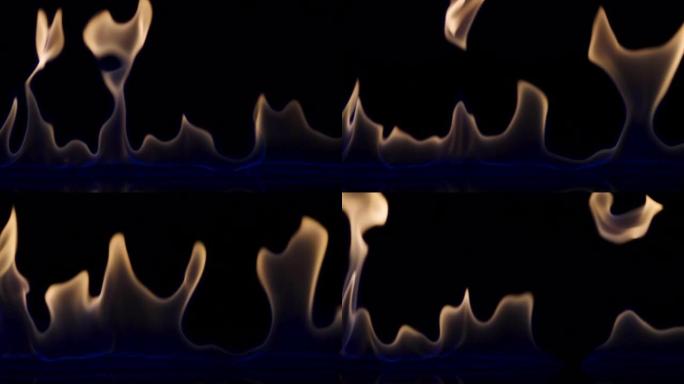 黑色反光背景上的易燃液体或汽油污渍闪烁并点燃。一场大火，燃烧的舌头在蓝光中燃烧，特写，慢动作。燃烧火