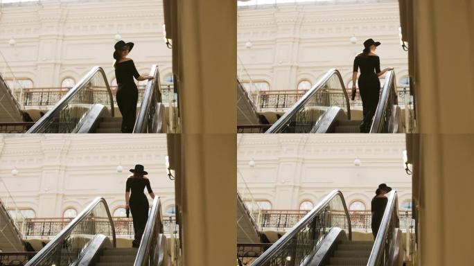 穿着黑色连衣裙的时尚女人走上自动扶梯，转身回头微笑。第一场景概念。慢动作