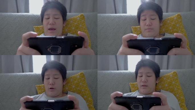 亚洲男孩在家坐在沙发上玩智能手机在线游戏，生活方式概念。