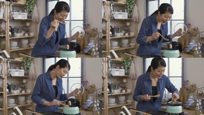 尝试从锅中品尝美味汤的亚洲女性对味道感到满意，并在将盖子放回家里的厨房之前先将汤匙上的液体沥干。
