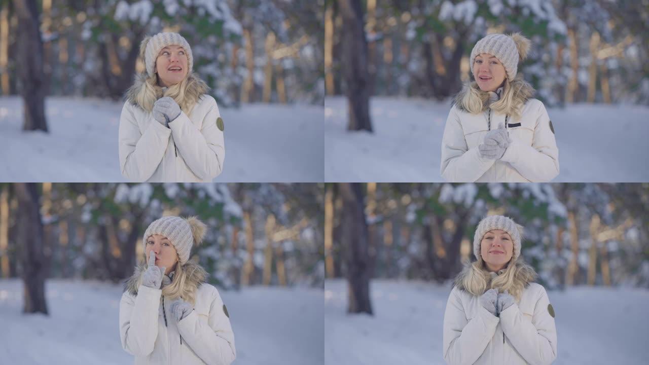 穿着暖和冬装的可爱女孩的肖像谈论一些事情，然后做一个安静的手势，秘密。年轻女子在白雪皑皑的森林模糊背