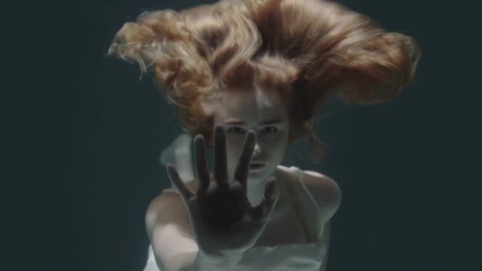 美丽的红发女孩在镜头前停在水下，僵住了