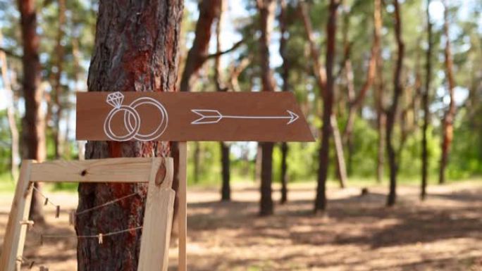 仪式场地上有结婚戒指的木制箭头标志。婚礼派对横幅帖子。户外松树林客人的方向信息横幅。乡村风格或乡村风