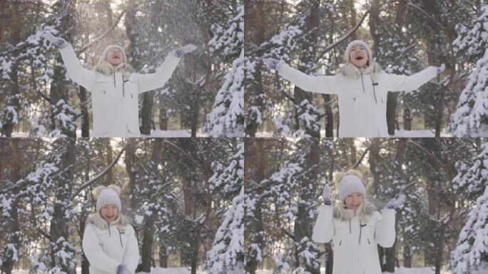 快乐可爱的女孩，穿着冬衣，抛起雪花，开心地笑。下雪的冬天，阳光灿烂。美丽的模糊背景雪域自然松林。缓慢