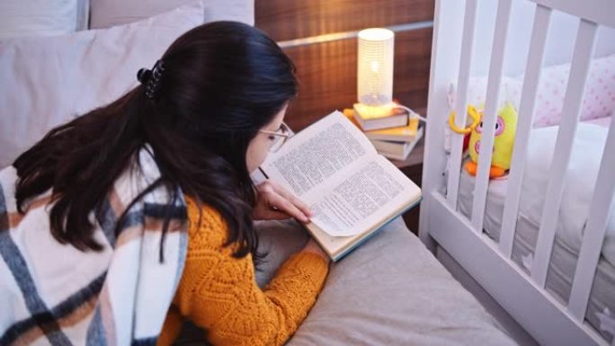 女人在卧室里看书，背景是婴儿床，特写镜头。