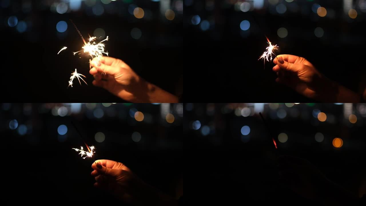 庆祝圣诞节和新年。在远处的房屋灯光下，用手在黑暗中握着烟火。4k视频