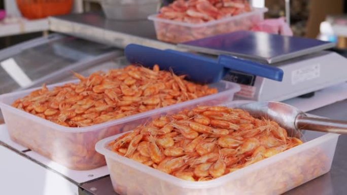 煮沸的红虾躺在塑料盒中，在市场上的露天柜台上出售