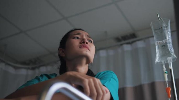 穿着医院礼服的亚洲妇女闭上眼睛，独自在医院的床上抽泣。她感到沮丧和担心。