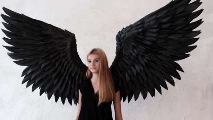 黑色天使翅膀和白色背景上的黑色连衣裙的女孩。