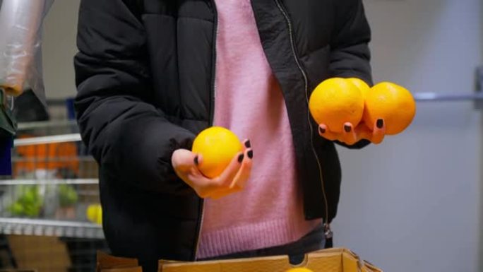 女孩的手在大卖场的货架上选择新鲜的橙子。选择性聚焦