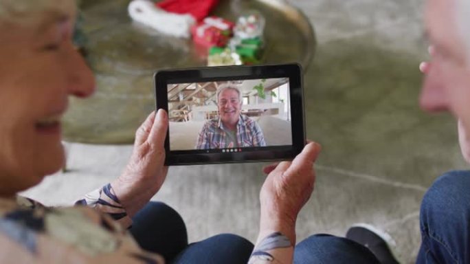 白人高级夫妇微笑着使用平板电脑与屏幕上的男人进行圣诞节视频通话
