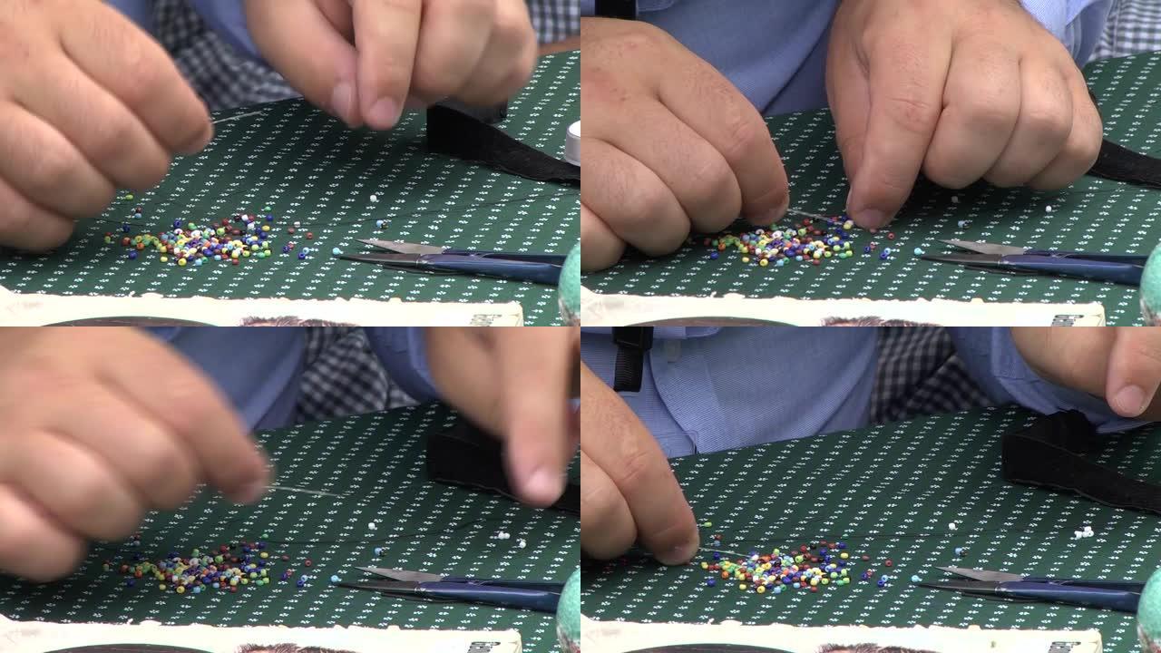 男人的手用针从桌子上的一堆里摘彩色珠子，他放在一边的白色珠子71