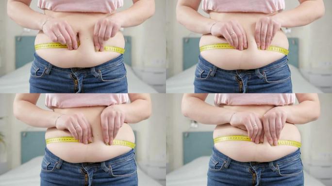 体重过重的年轻胖女人用卷尺测量她的大肚子。节食的概念，不健康的生活方式，超重和肥胖