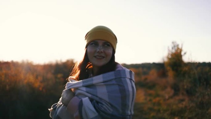 迷人的女性在大自然中放松。快乐自由的女人戴着黄色的帽子和舒适的衣服，配羊绒围巾，在户外享受秋天公园的