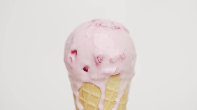 特写，将草莓味的冰淇淋融化在蛋筒上。