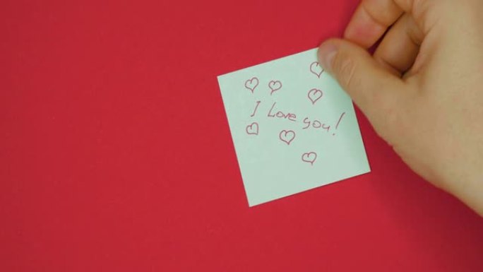 男手贴上写着 “我爱你” 的贴纸是用笔写的，用红色背景的情人节用心画的