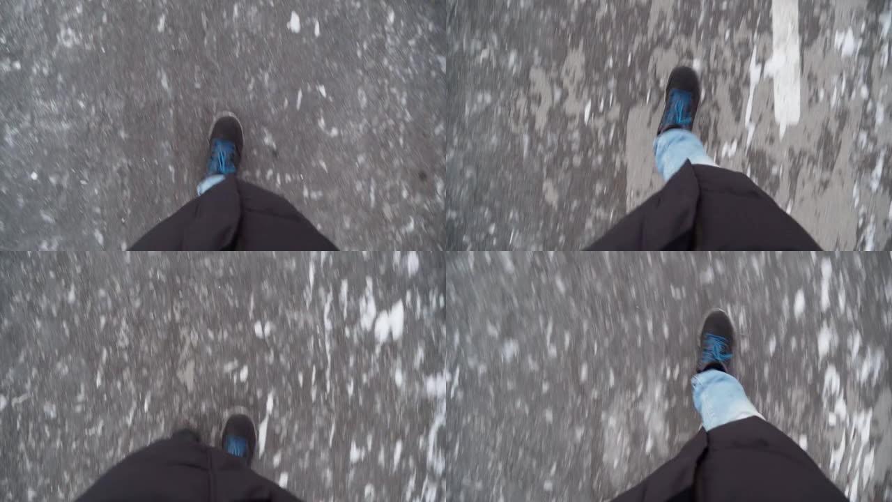 冬天，一个穿着黑色靴子和牛仔裤的男人的腿在街上滑溜溜的冰上行走。视点视频