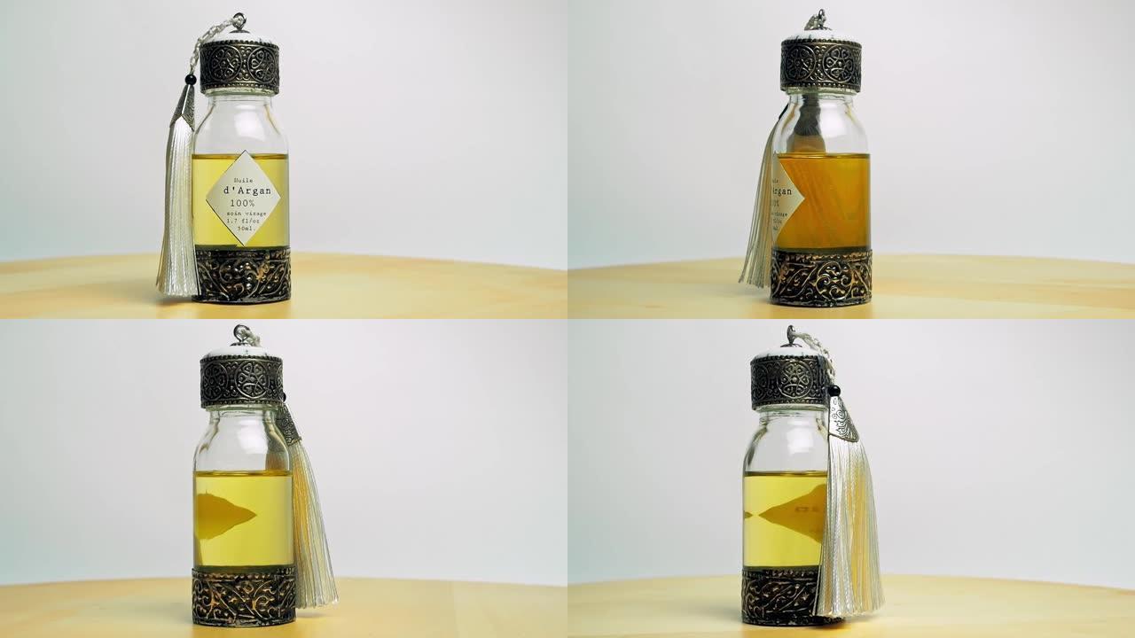 东方玻璃和金属瓶中的摩洛哥坚果油在木制桌子和白色背景上运动
