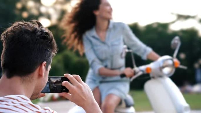 男子用手机在滑板车户外拍女友照片