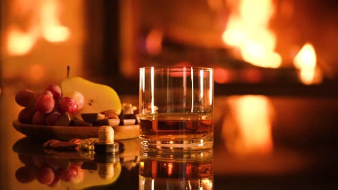 一杯威士忌和一盘巧克力，葡萄，梨在壁炉背景上。