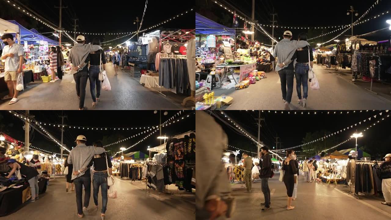 游客在泰国夜市散步购买食物，周末度假穿衣服。