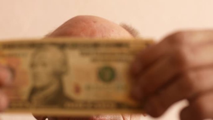 一位70岁的白人老人戴着眼镜，仔细检查了一张10美元的钞票。假钱主题。一个人手中的10美元。选择性聚