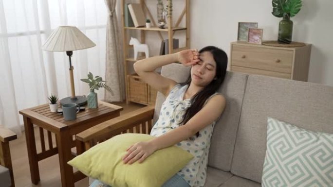 疲惫的亚洲女孩在午睡时间在家里的客厅里用枕头在沙发上伸展和向后倾斜很快就睡着了。