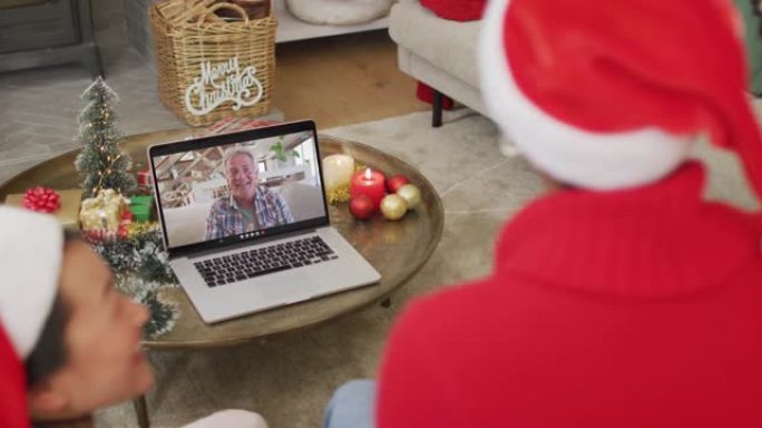 拥有圣诞老人帽子的多元化家庭使用笔记本电脑进行圣诞节视频通话，屏幕上有快乐的男人