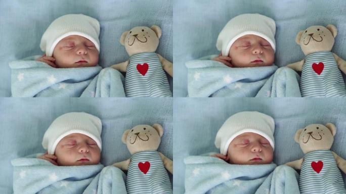 初生婴儿脸部肖像的特写镜头早期与蓝色背景上的塔迪熊睡觉。孩子在帽子上生命的开始。婴儿，分娩，出生的最
