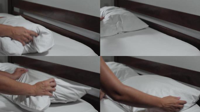 女人的手敲打枕头。一个无法辨认的女人在家里或旅馆的房间里用白色亚麻布铺床。