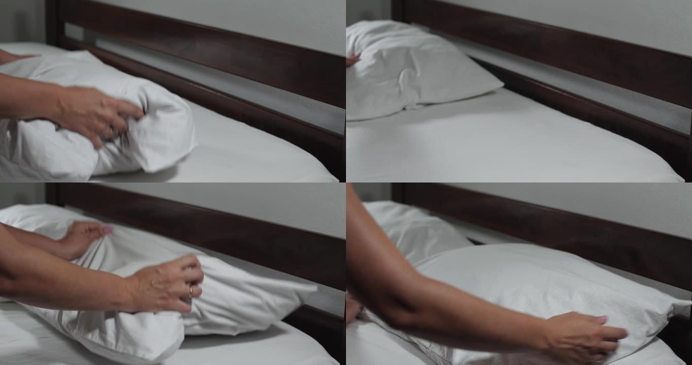 女人的手敲打枕头。一个无法辨认的女人在家里或旅馆的房间里用白色亚麻布铺床。