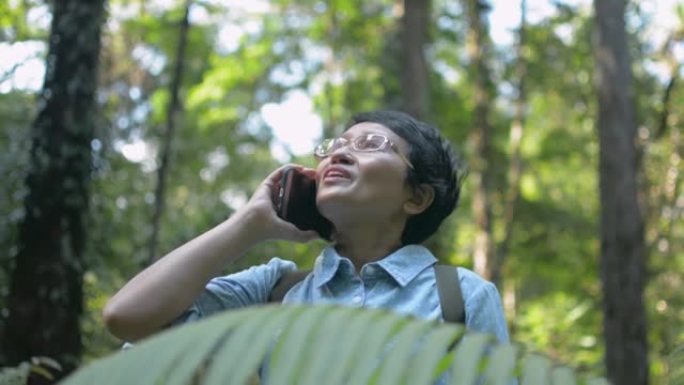 亚洲女性自然探险家在森林中徒步旅行时使用移动智能手机与家人交谈。