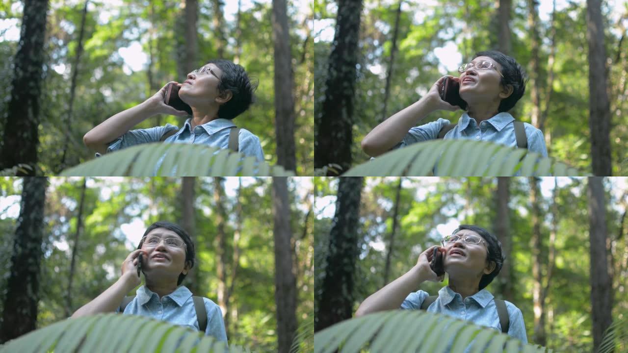 亚洲女性自然探险家在森林中徒步旅行时使用移动智能手机与家人交谈。