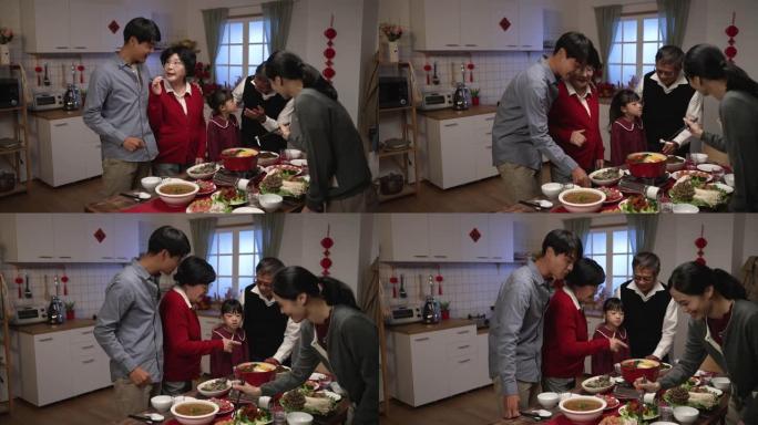 开朗的亚洲老母亲穿着红色衣服和儿子说话，而儿媳在餐桌上用筷子准备火锅。准备农历新年团圆饭