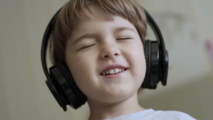 孩子戴着耳机闭着眼睛放松时的慢动作。孩子在家听音乐。戴着耳机听音乐的可爱的小男孩的肖像。快乐无忧无虑