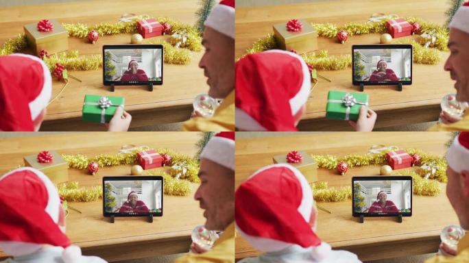 白人父亲和儿子戴着圣诞老人的帽子，使用平板电脑与屏幕上的女人进行圣诞节视频通话