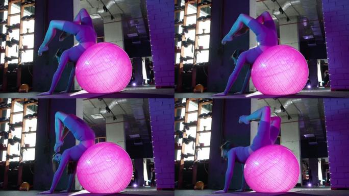 年轻女子在做普拉提 -- 坐在霓虹灯的健身球上锻炼
