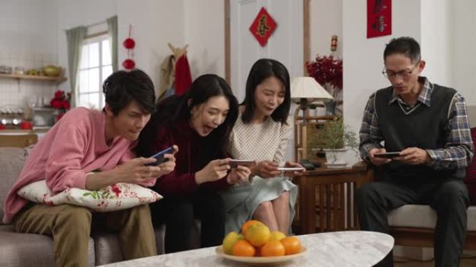 春节期间，全家人在客厅玩激动人心的手机游戏，亚洲妈妈问女儿如何玩。背面的中文文本翻译: 春天和祝贺