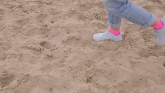 穿着粉红色袜子和白色运动鞋的妇女的脚在沙滩上迈出了一步。