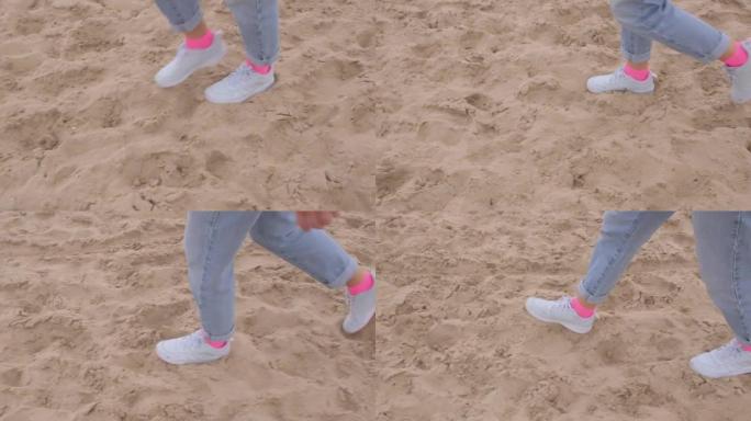 穿着粉红色袜子和白色运动鞋的妇女的脚在沙滩上迈出了一步。