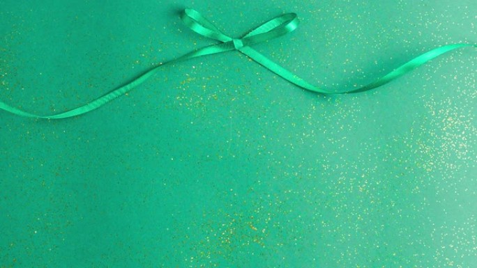 翠绿色缎带蝴蝶结，系在绿色上，金色闪光。停止运动动画圣诞节假期和呈现概念平与复制空间。