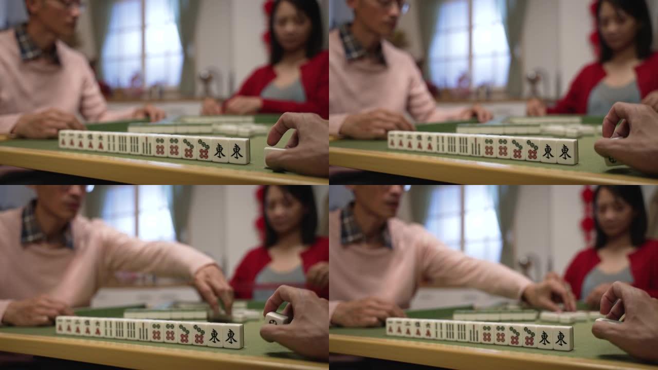 特写与选择性焦点的一个玩家的手玩瓷砖旁边的麻将棋子的手，而他的家人正在有他们的回合。中文翻译:东方