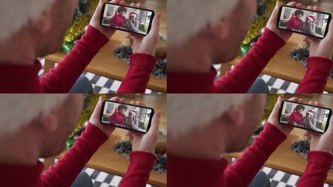 戴着圣诞老人帽子的白人男子使用智能手机进行圣诞节视频通话，屏幕上有微笑的家人