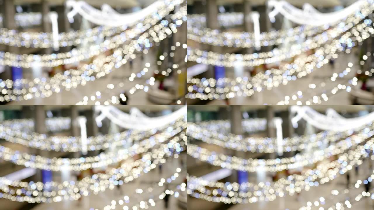 室内的天花板上悬挂着发光灯泡。这些装饰品在圣诞节时使用。模糊的背景是人们进入或离开建筑物。从右向左倾