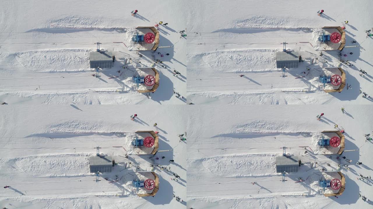 滑雪升降机底部站的空中俯视图。升降机轮在旋转，滑雪者乘滑雪缆车上升。