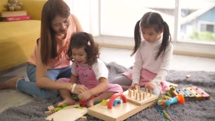 亚洲妇女周末快乐，看着她的婴儿在客厅里玩玩具，积木