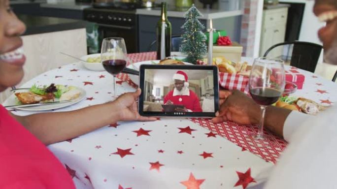 非裔美国人夫妇与葡萄酒使用平板电脑与圣诞老人在屏幕上进行圣诞节视频通话