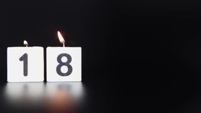 一根方形蜡烛，上面写着数字18被点燃并吹出，庆祝生日或周年纪念日。